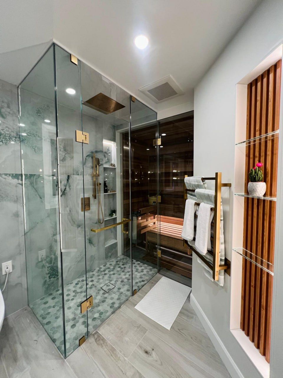 Glass steam shower with wet-marble tile beside a cedar sauna