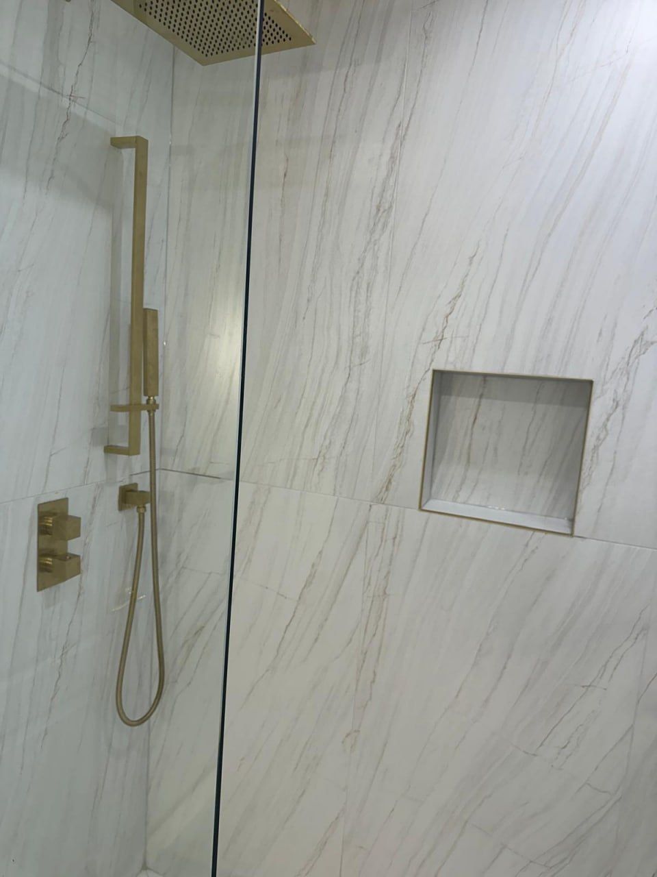 White marble shower with brushed gold fixtures and niche