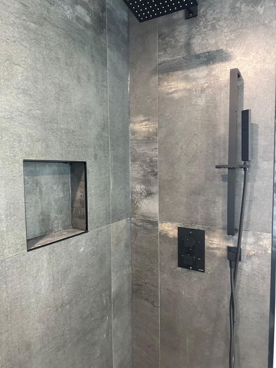 Concrete-look shower with matte black fixtures and niche
