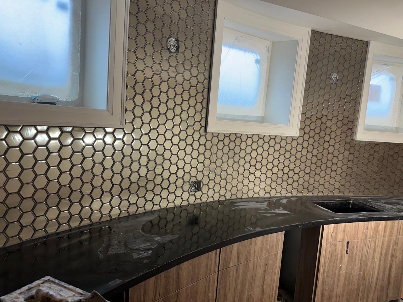 Beige hexagon mosaic backsplash with wood cabinetry and black counter