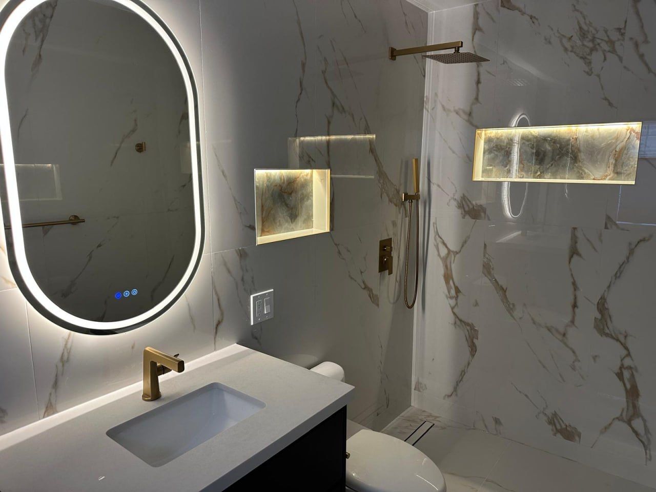 Calacatta marble ensuite with backlit onyx niches and gold fixtures