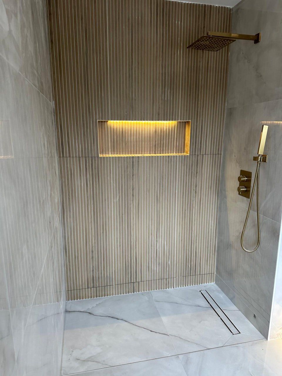 Fluted-tile walk-in shower with backlit niche and gold fixtures