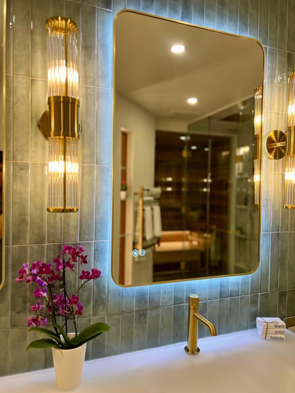 Green-tile vanity with brass sconce, LED mirror and orchid