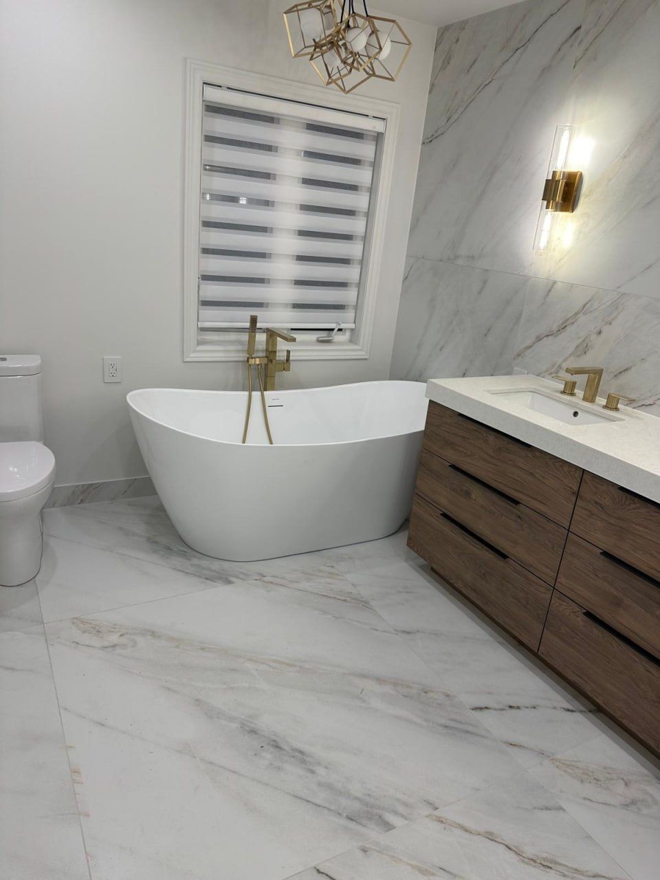 Marble bathroom with freestanding tub and gold geometric chandelier