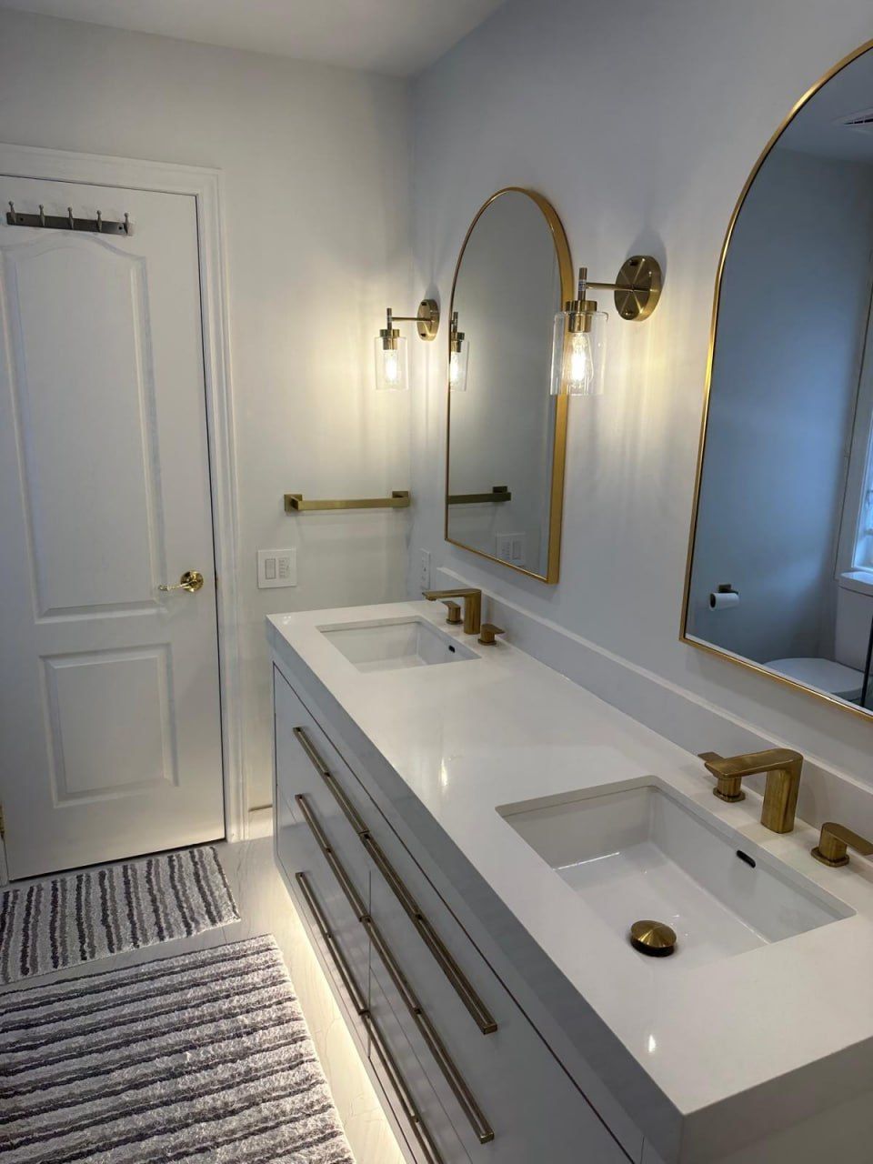 Grey vanity with gold fixtures and arched mirrors