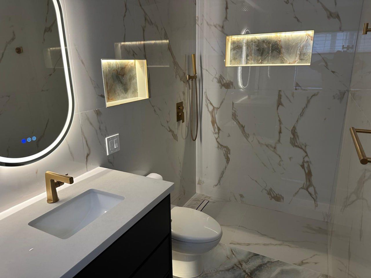 Marble ensuite with black vanity, gold fixtures and backlit onyx niches