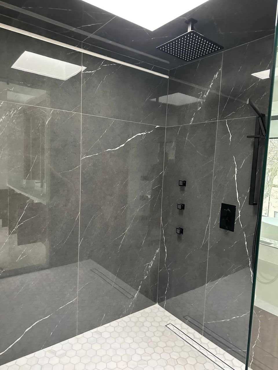 Dark marble shower with matte black body jets and hex floor